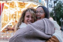Lachende Freundinnen umarmen sich gegen beleuchtetes Karussell — Stockfoto