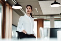 Confident female entrepreneur standing in illuminated office — Stock Photo