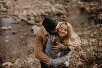 Hipster man with knit hat kissing girlfriend in forest — Stock Photo
