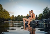 Молодая пара сидит на купальной платформе на озере и смотрит на расстояние — стоковое фото