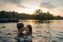 Young couple swimming in lake, kissing at sunset — Stock Photo