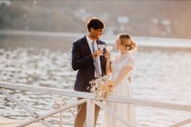 Newlywed couple toasting champagne while standing by railing during wedding ceremony — Stock Photo