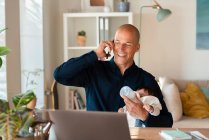 Père souriant parlant sur un téléphone intelligent tout en donnant du lait à sa fille à la maison — Photo de stock