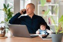 Père parlant sur le téléphone intelligent tout en tenant bébé fille à la maison — Photo de stock