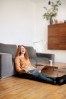 Full length of cheerful woman laughing while sitting with laptop in living room at home — Stock Photo