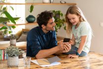 Homme montrant téléphone intelligent à la fille tout en discutant à la maison — Photo de stock