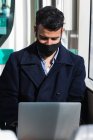 Young businessman wearing protective face mask using laptop while sitting in train — Stock Photo