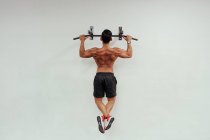 Deportista adulto haciendo flexiones de mentón con equipo de ejercicio en la pared blanca - foto de stock