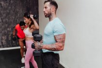 Deportista sosteniendo la mancuerna mientras está de pie con amigos haciendo ejercicio en el gimnasio - foto de stock