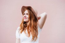 Sorridente rossa donna in piedi di fronte al muro rosa, mentre guardando altrove — Foto stock