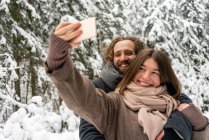 Усміхнена жінка бере селфі з чоловіком через мобільний телефон, стоячи в лісі — стокове фото