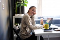 Sorrindo mulher sentada por laptop no escritório em casa — Fotografia de Stock