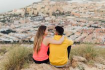 Young girlfriend sitting with arm around of boyfriend on hill — Stock Photo