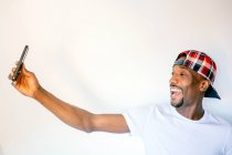 Cheerful man wearing plaid cap taking selfie through mobile phone against white background — Stock Photo