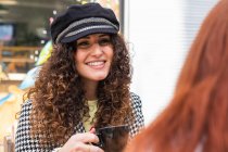 Mujer usando gorra tomando café con amigos en el café de la acera - foto de stock