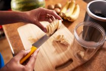 Femme coupant banane sur planche en bois dans la cuisine — Photo de stock
