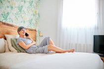 Mature woman talking on smart phone while sitting in bedroom at home — Stock Photo
