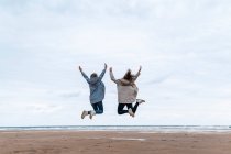 Amici femminili spensierati che saltano con le braccia alzate in spiaggia — Foto stock