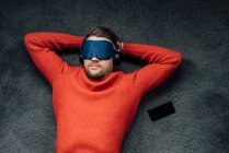 Maschio pisolino professionale con maschera oculare durante l'ascolto di musica attraverso le cuffie sul posto di lavoro — Foto stock