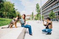 Homme photographiant femme assise par chien par téléphone portable en ville — Photo de stock