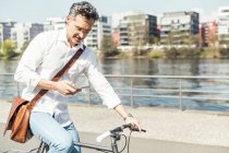 Empresario usando teléfono móvil mientras pedalea en bicicleta en un día soleado - foto de stock