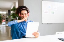 Empresaria con la mano en la barbilla usando tableta digital en la oficina creativa - foto de stock