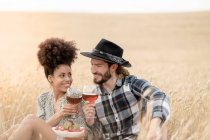 Couple toasting drink while sitting on field during picnic — Stock Photo