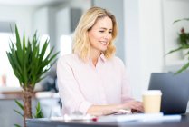 Smiling businesswoman working on laptop at home office — Stock Photo