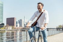 Sonriente hombre de negocios maduro de pie con bicicleta en la ciudad - foto de stock