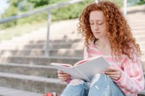 Donna rossa con capelli ricci libro di lettura mentre seduto sulle scale — Foto stock