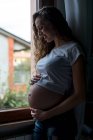 Donna incinta sorridente in piedi con le mani sullo stomaco a casa — Foto stock