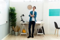 Hombre de negocios seguro con los brazos cruzados de pie en la oficina creativa - foto de stock