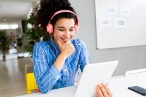 Emprendedora con auriculares trabajando en tableta digital en oficina creativa - foto de stock