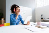 Mujer emprendedora sonriente con auriculares usando tableta digital en la oficina - foto de stock
