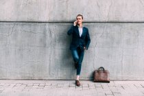 Бизнесмен разговаривает по мобильному телефону, стоя у портфеля на пешеходной дорожке — стоковое фото