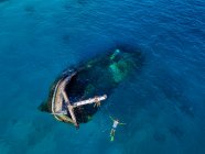 Aerial view of lone man snorkeling around sunken shipwreck — Stock Photo