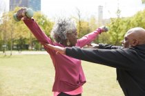 Uomo che assiste la donna anziana che si allena con i manubri al parco — Foto stock