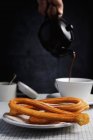 Plate of churros with hand of man pouring hot chocolate in background — Stock Photo