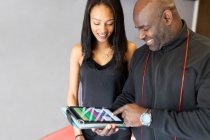 Smiling male fitness instructor showing digital tablet to young woman — Stock Photo