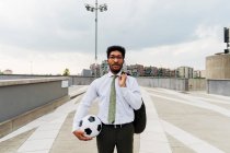 Homme d'affaires tenant ballon sportif et blazer tout en se tenant sur le sentier — Photo de stock