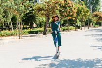 Donna sorridente guardando lontano mentre cavalcava scooter elettrico spinta al parco durante la giornata di sole — Foto stock
