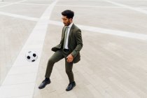 Homme d'affaires jouant avec le ballon de football sur le sentier piétonnier — Photo de stock
