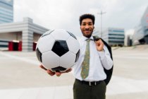 Jeune homme d'affaires montrant un ballon de football debout sur un sentier piétonnier — Photo de stock