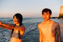 Männliche und weibliche Freunde schauen weg, während sie bei Sonnenuntergang am Strand stehen — Stockfoto