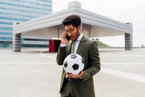 Homme professionnel tenant ballon de football tout en parlant sur téléphone mobile — Photo de stock