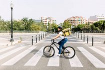 Consegna donna che trasporta la borsa del corriere mentre guida in bicicletta su strada — Foto stock