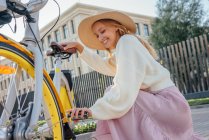 Femme souriante portant un chapeau réparant la chaîne de vélo — Photo de stock