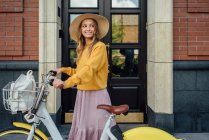 Красива жінка, дивлячись геть, стоячи з велосипедом перед дверима — стокове фото