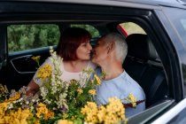Romantic senior couple sitting with tansy flowers while kissing in car — Stock Photo