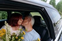 Affectionate couple kissing while sitting with bunch of flowers in car — Stock Photo